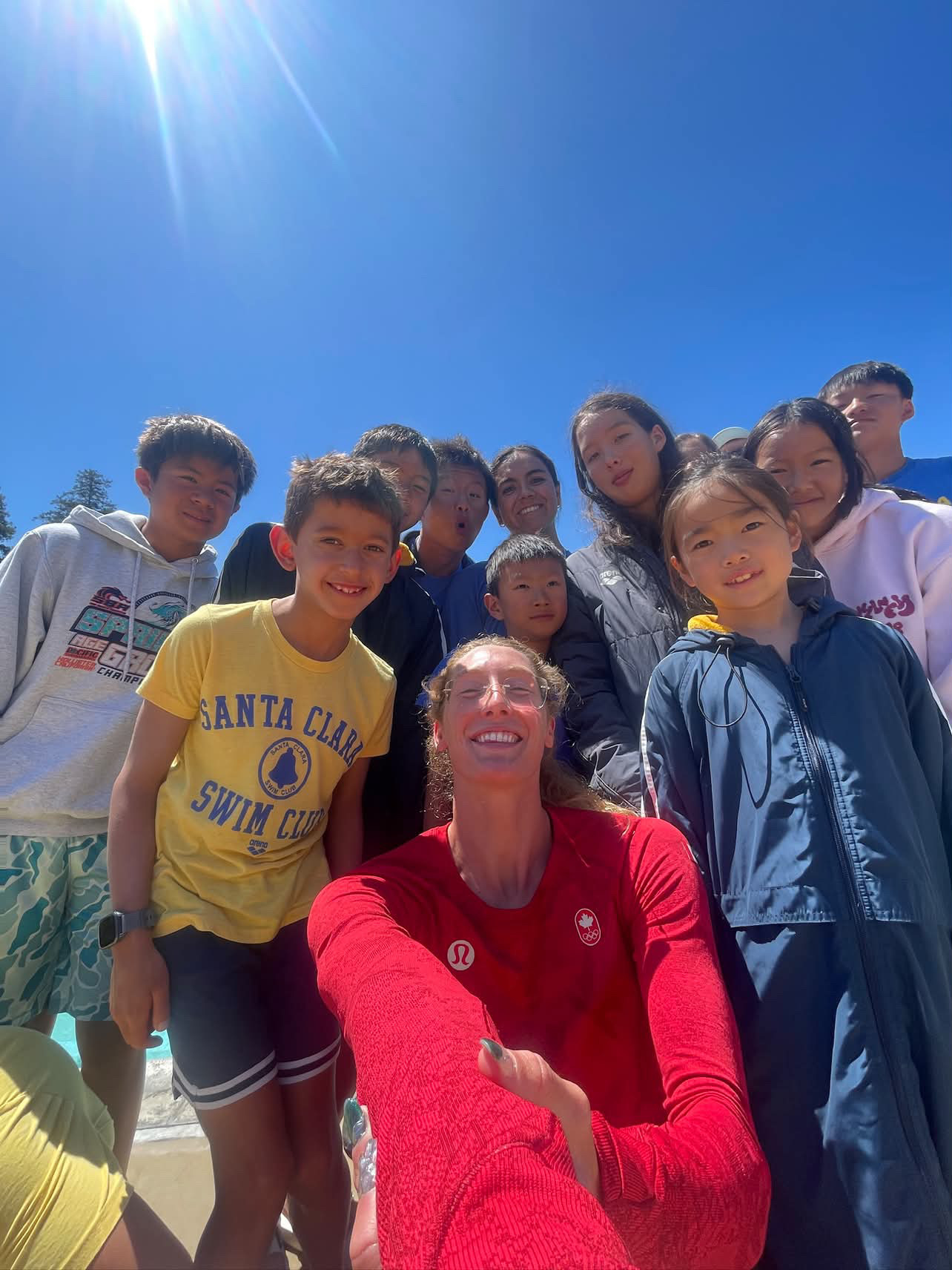 Taylor Ruck taking a group selfie with young swimmers at a swim clinic